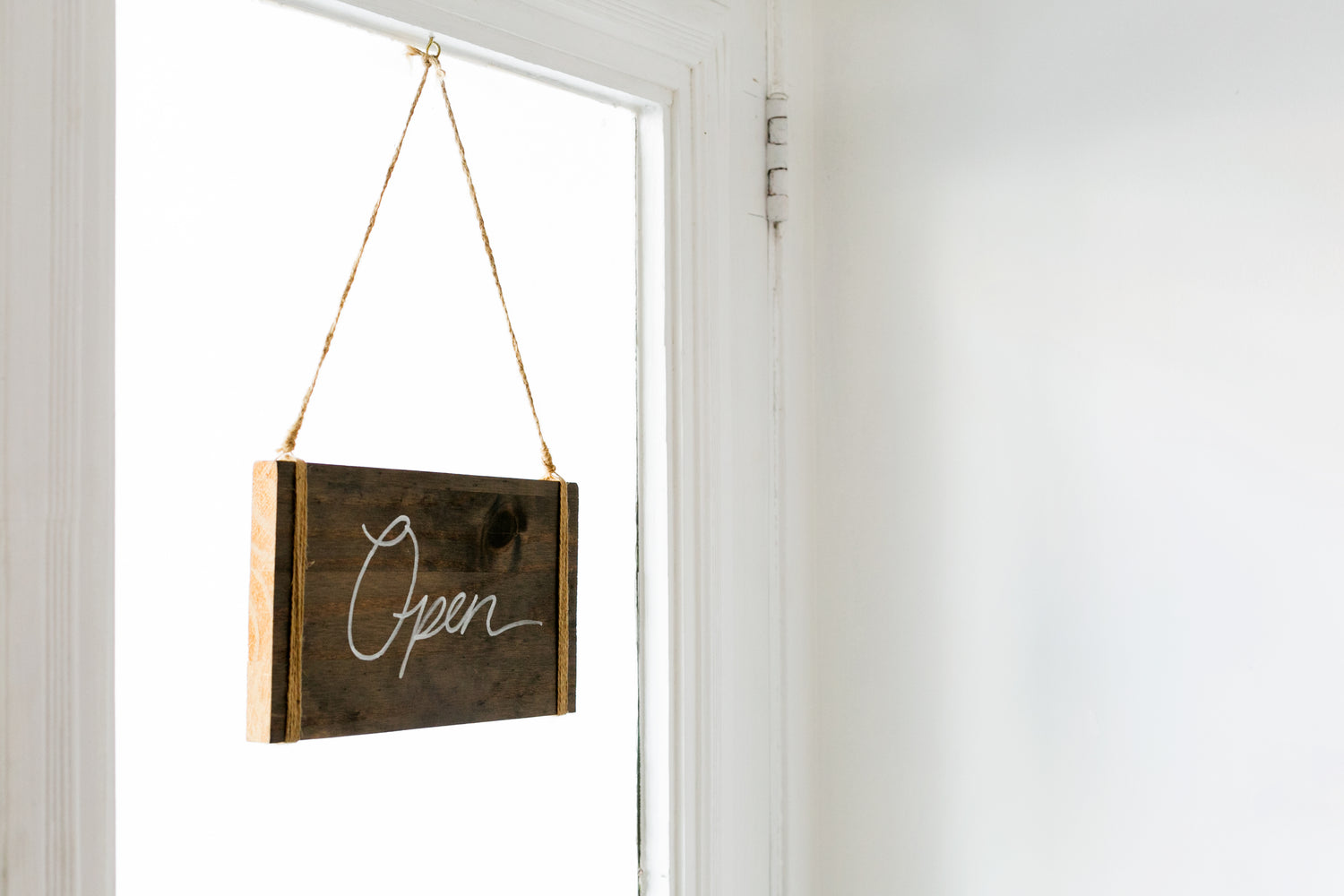 Image of wooden and hand written open sign hanging in a window with a bright white background on a door