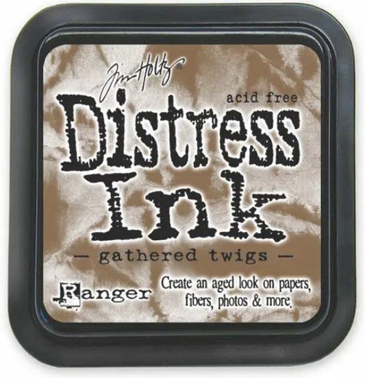 A square Tim Holtz Distress Ink pad in the shade gathered twigs, featuring a black plastic casing and a textured brown paper label inside.